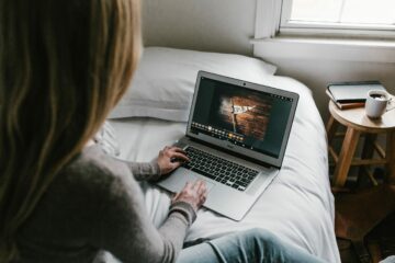disabled neurodivergent graduate sat on her bed, typing on a laptop positioned in front of her