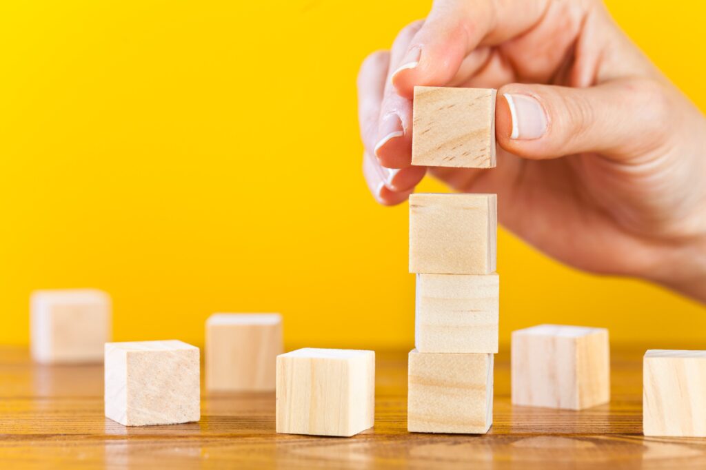 a hand putting small wooden building blocks into a tower, symbolising baby steps