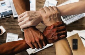 four hands in a square holding on to each other's wrists, representing a range of ethnicities, representing diversity information in job listings