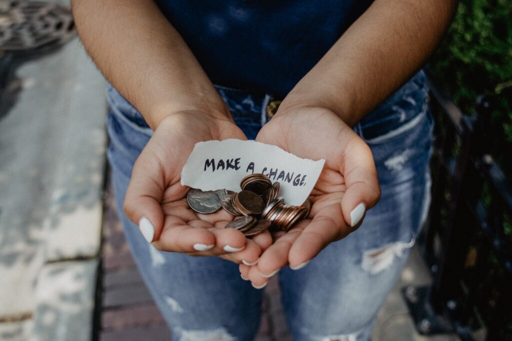 hands holding loose coins and a sign that says 'make a change', to symbolise the astriid challenge